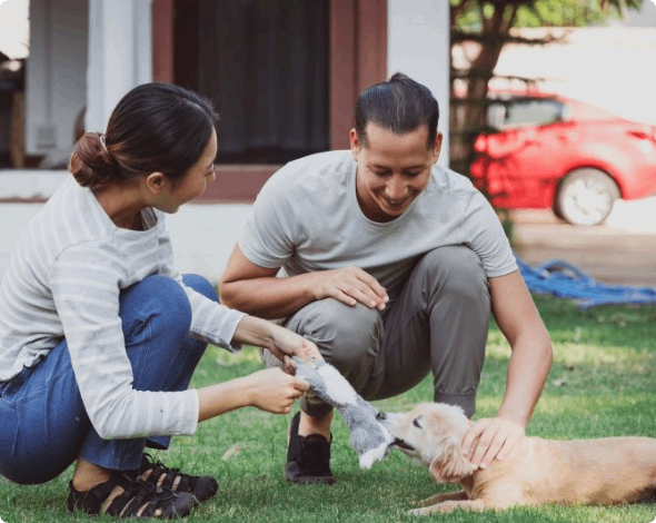 Two people playing with a puppy in a yard.