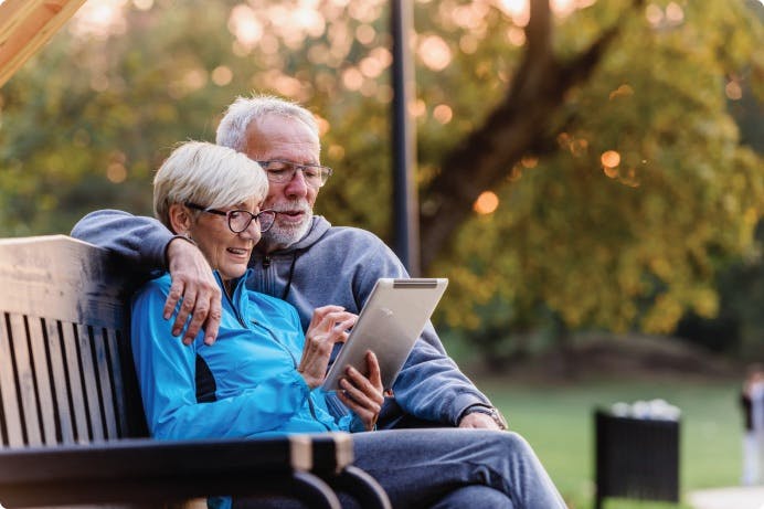 a man and woman sitting on a bench looking at a tablet