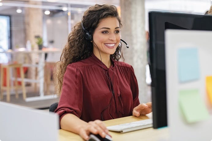 Woman with a headset on smiling and working in front of a computer