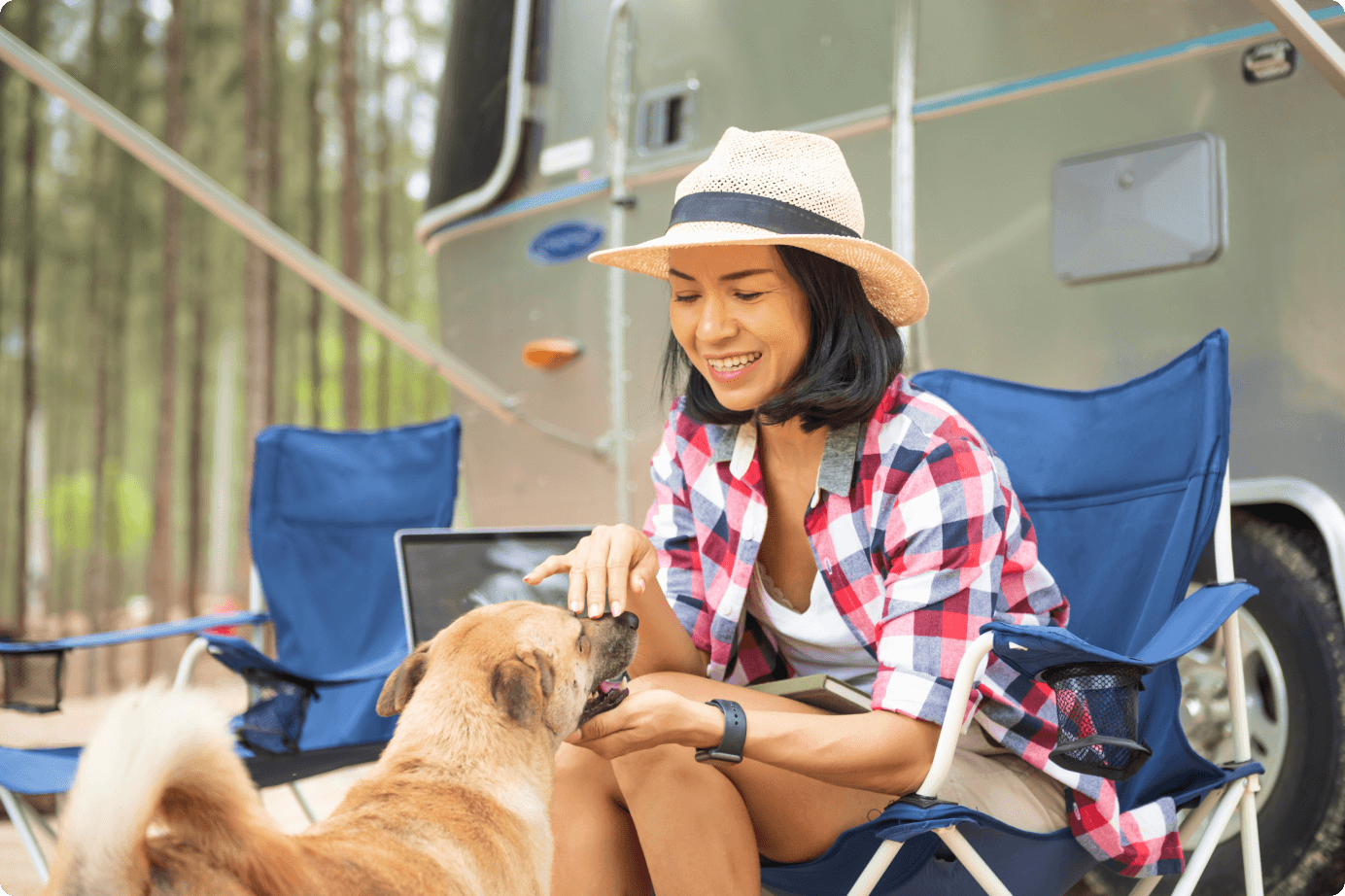 A woman sitting and playing with her dog outside a parked RV