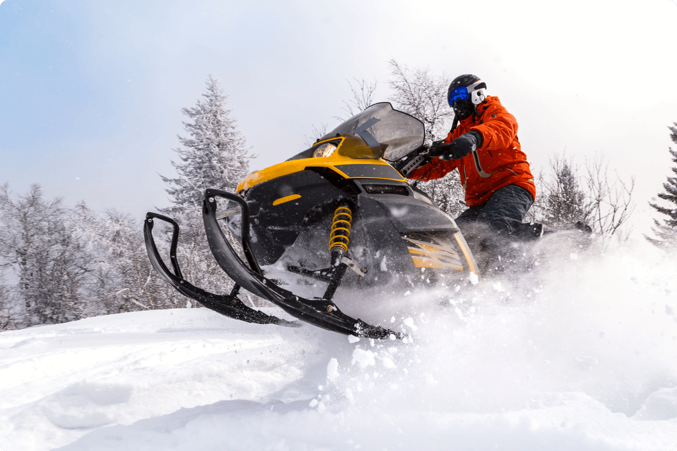 A snowmobile go over a snow mound at speed