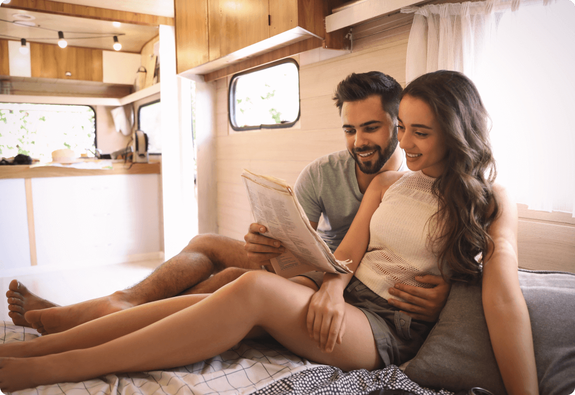 A young couple sitting and smiling in an RV reading an item