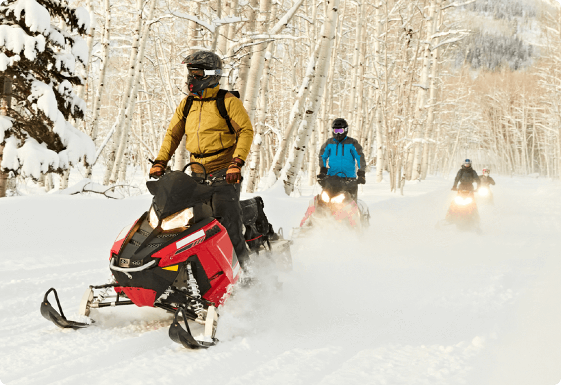 A group of people riding snowmobiles in the snow