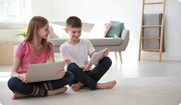 a boy and girl sitting on the floor looking at a laptop