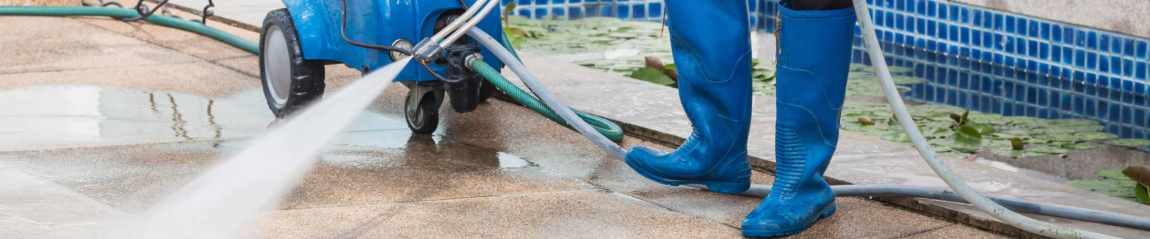 someone wearing rubber boots using a power washer on the ground