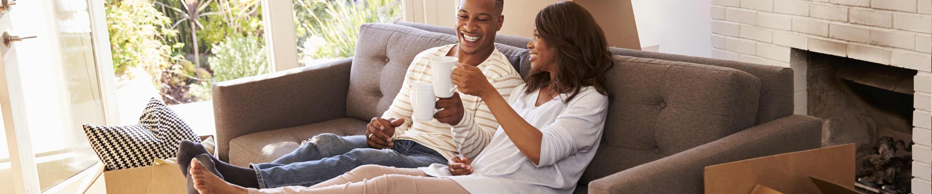 Young couple sitting on couch drinking coffee celebrating becoming home owners.