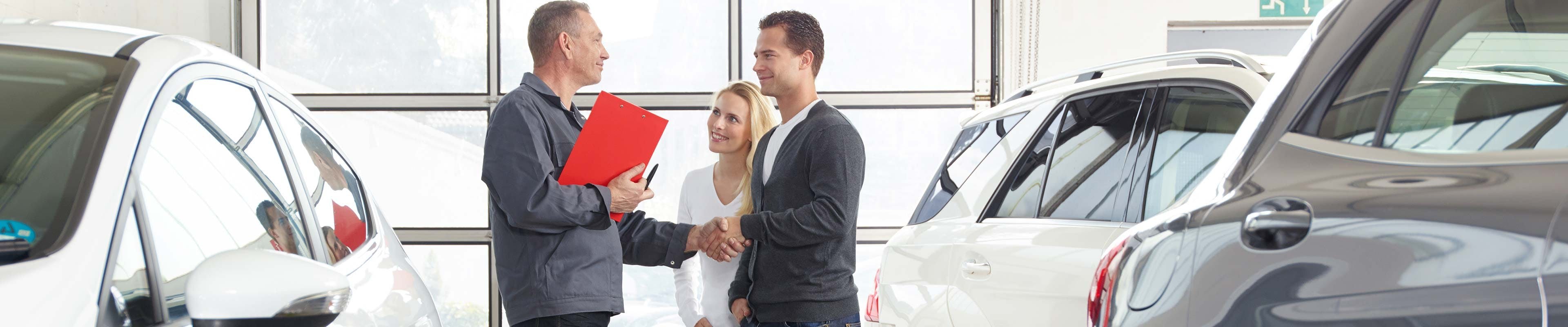 Image of a young couple working on the purchase of a car at a dealership with a car salesman.
