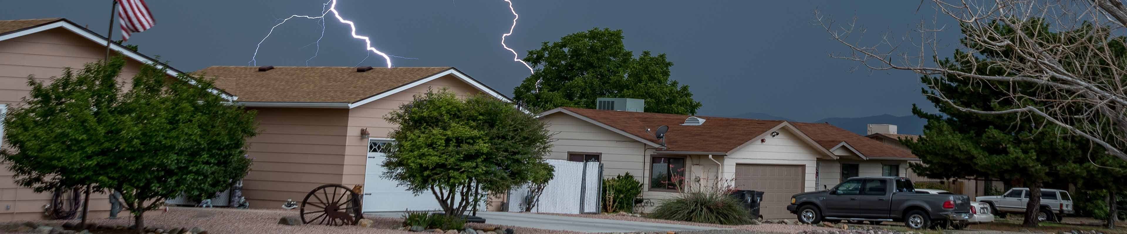 Image of homes in a neighborhood with lightning striking from above.