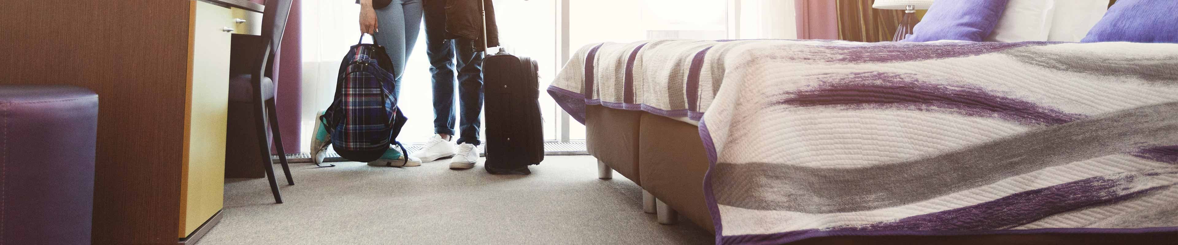 A couple stands in a hotel room with packed suitcases after being temporarily relocated from their damaged apartment.
