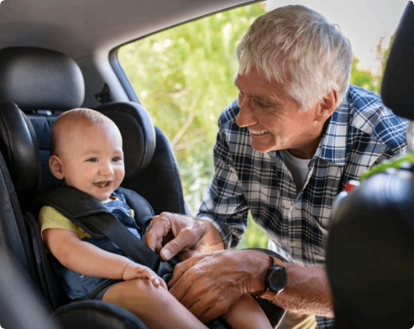Grandfather putting his grandchild into a car seat.