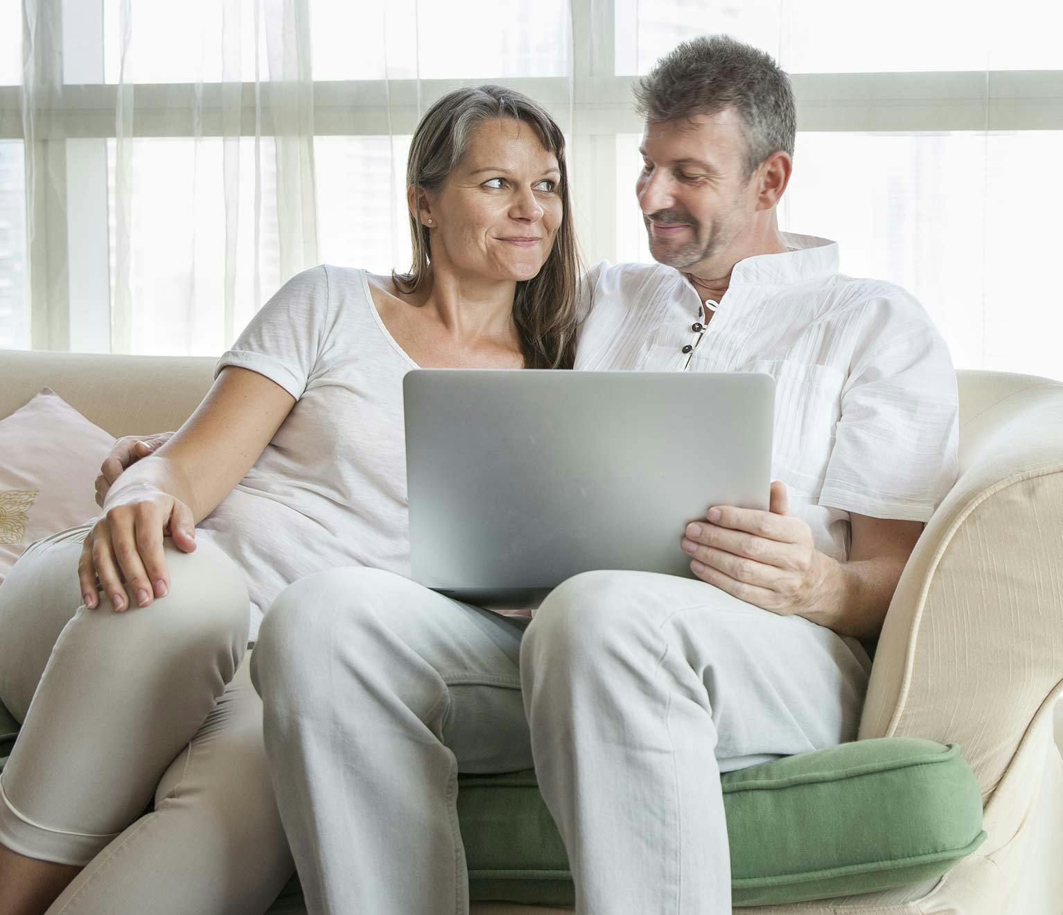 Middle-aged couple sitting on the couch researching ways to save on homeowners insurance.