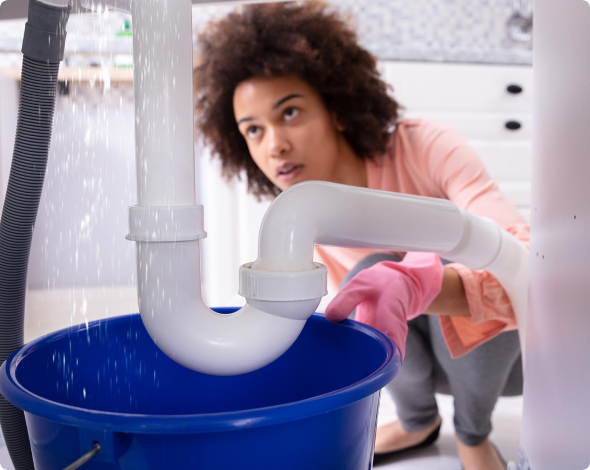a woman looking under her sink at a leaky pipe