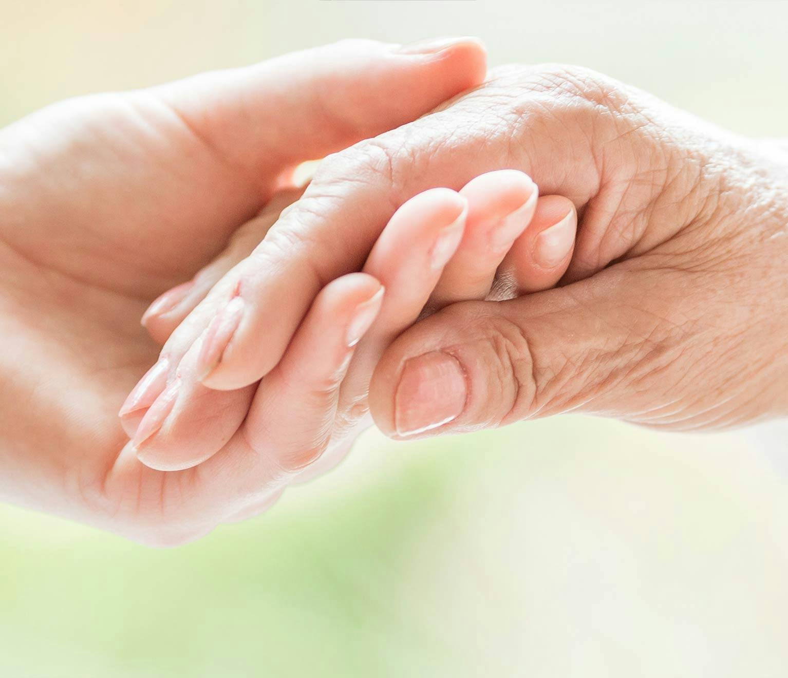 Respite caregiver holding hand of elderly patient.