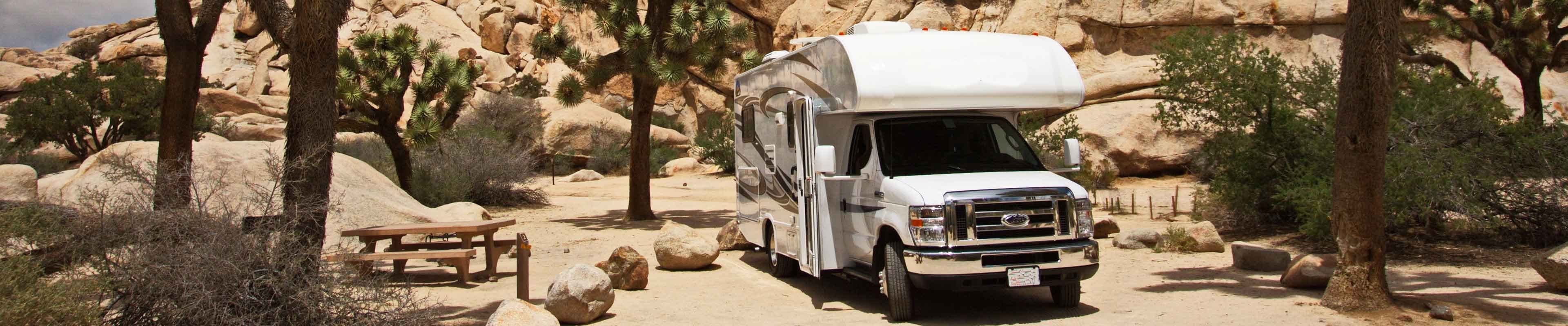 White, small recreational vehicle parked facing the camera at a desert campground in the Southwestern United States