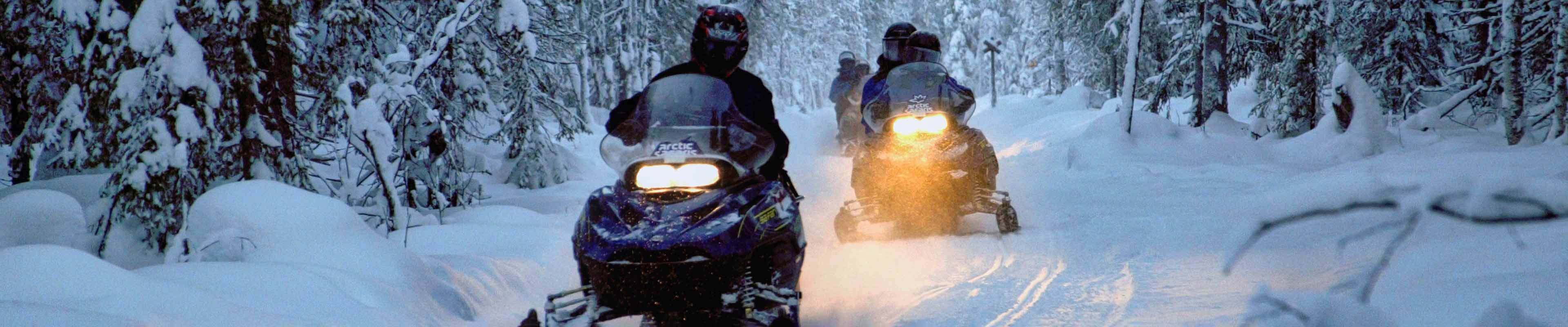 snowmobiles on a snowy trail at night 