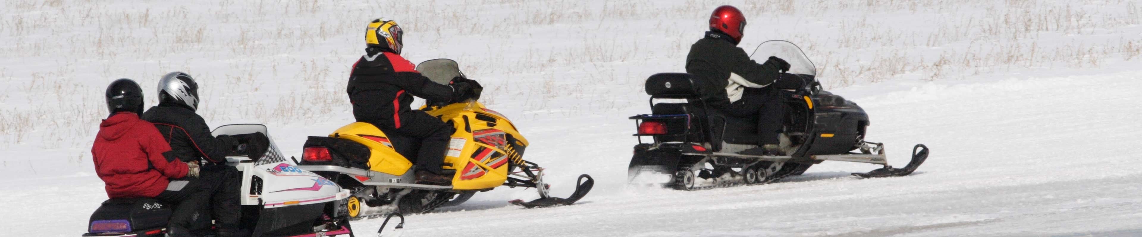 Snowmobilers riding down a snowmobile trail after a winter storm.