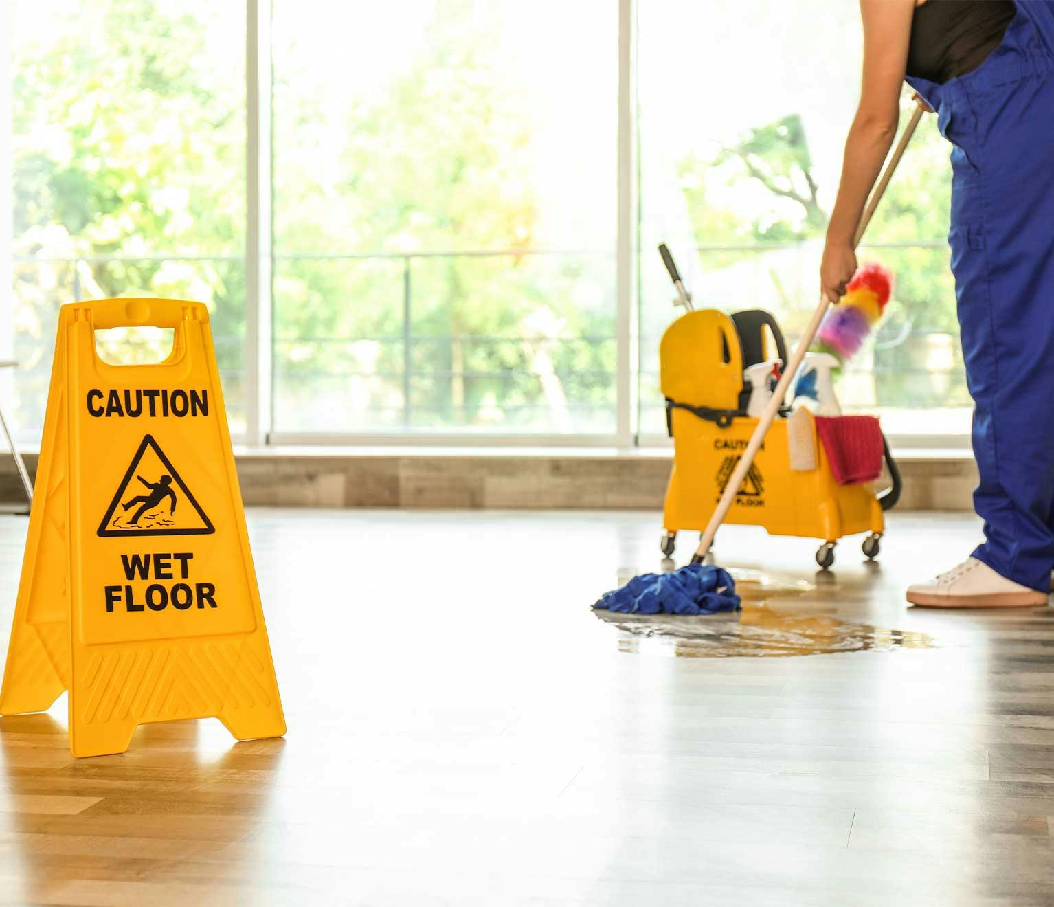 caution sign is posted warning others of a wet floor while a person mops_responsive