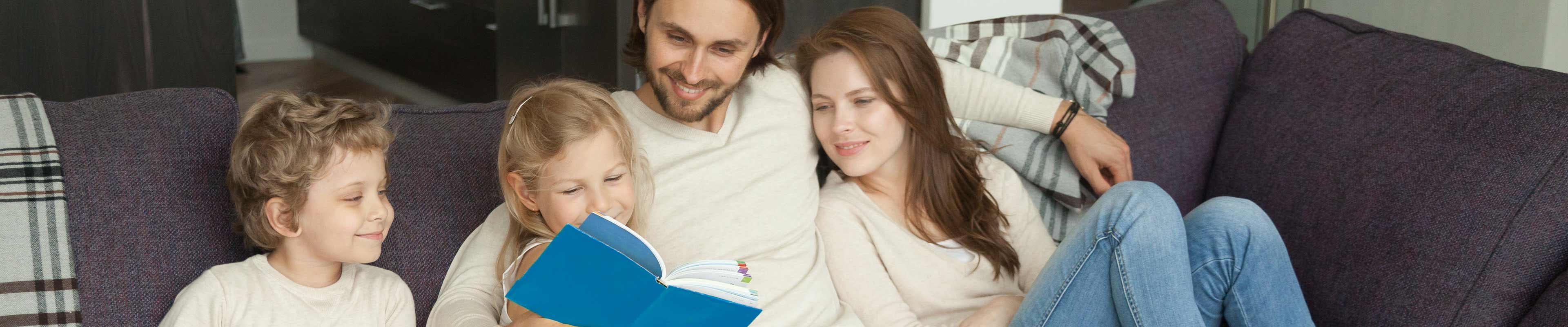 Image of a family on a living room couch reading a book together.