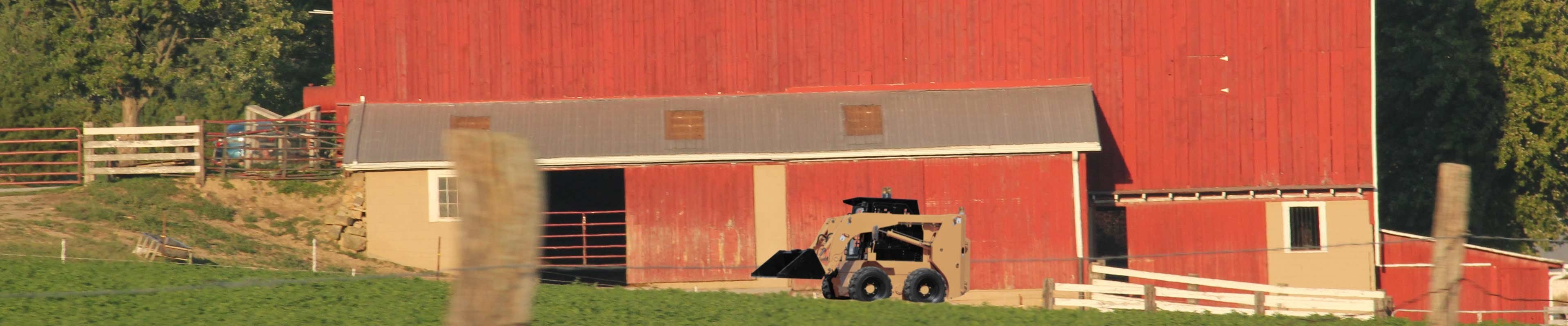 Image of a skid steer in front of a barn.