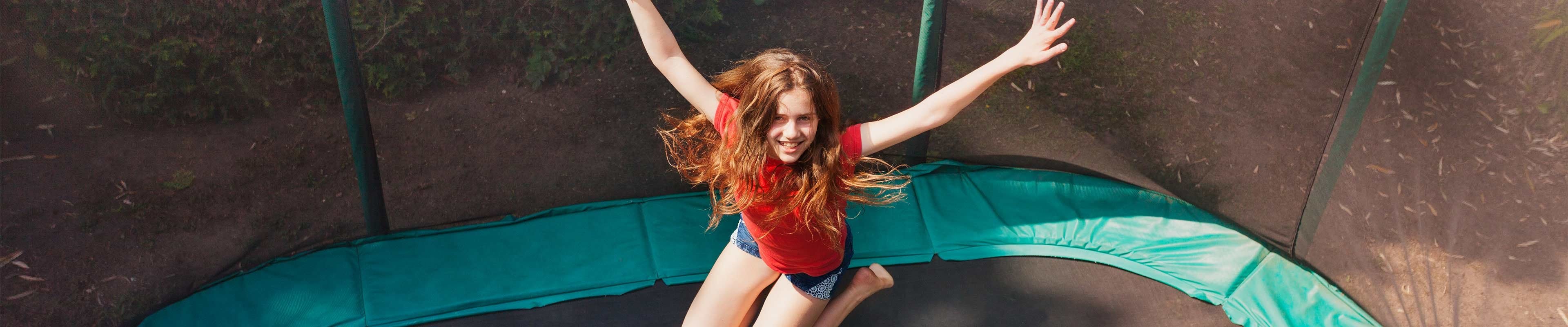 A little girl jumps safely on a trampoline.
