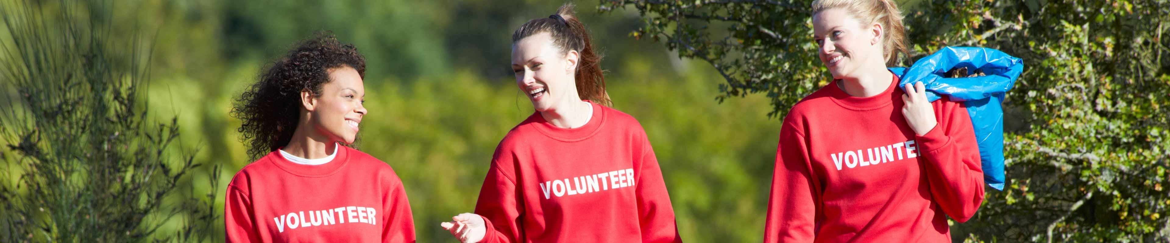 Three woman wearing red crewneck sweaters volunteering at a park.