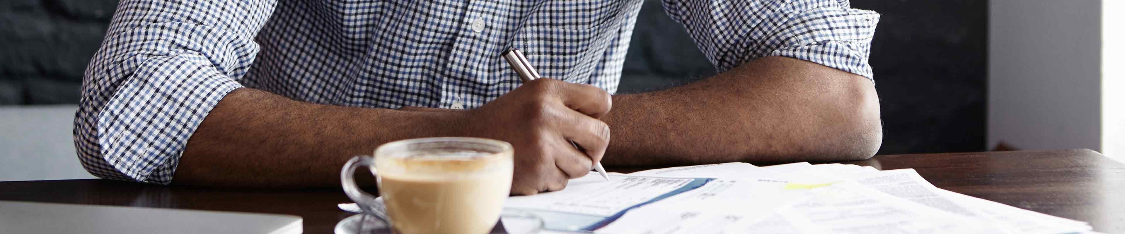 young black man sitting at a desk with a cup of coffee in front of him looking at paperwork