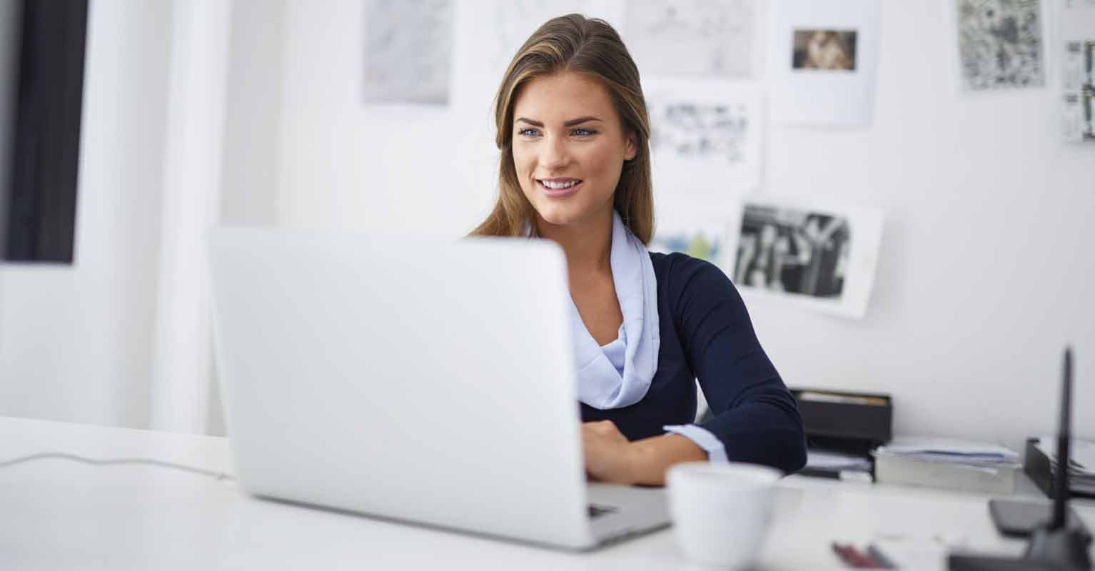 woman sitting at desk, looking at laptop computer and smiling