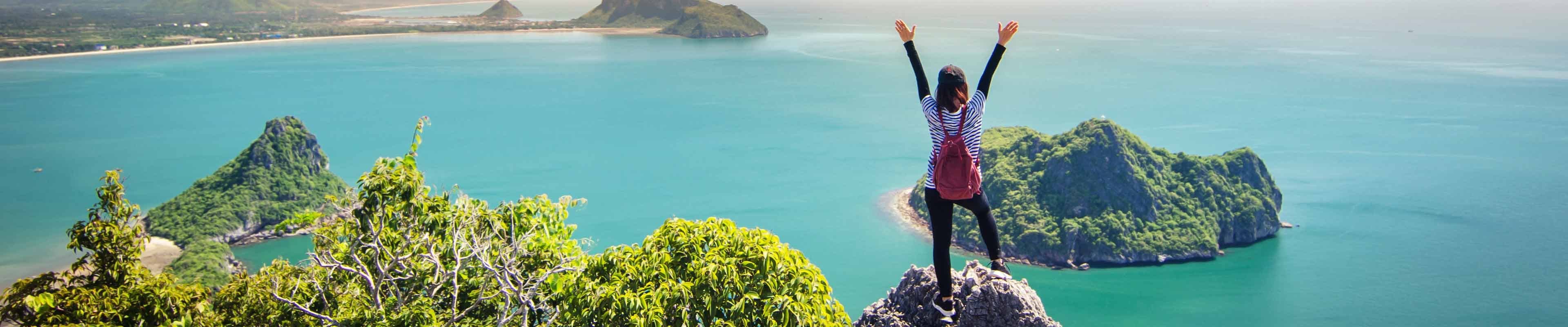Woman standing on mountaintop overlooking beautiful body of water while traveling.
