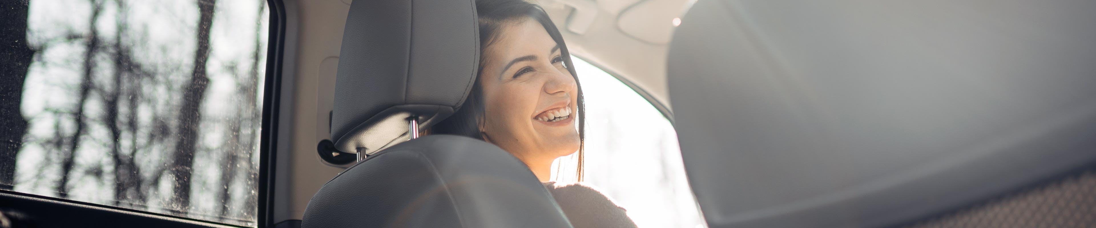 Happy young woman in driver's seat driving after purchasing the right amount of car insurance coverage.