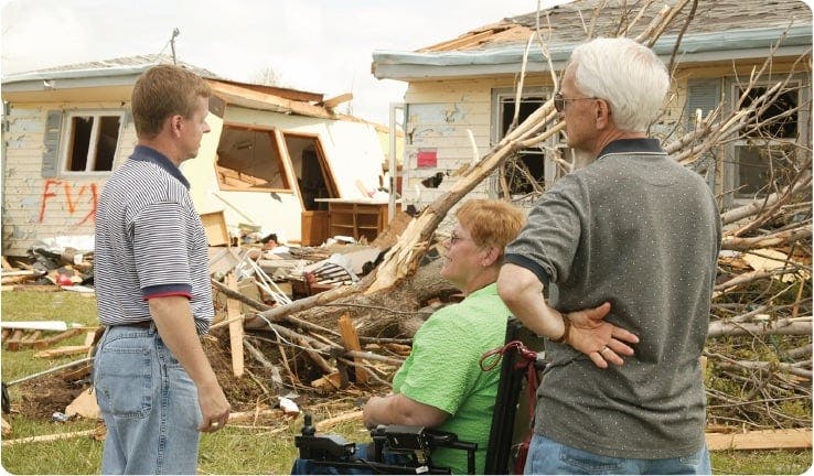 a man and a woman looking at a tree that fell on a house