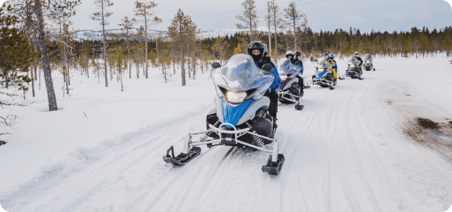 A group of people riding snowmobiles on a snowy road