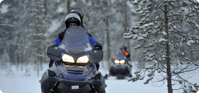A couple of people riding snowmobiles at dusk