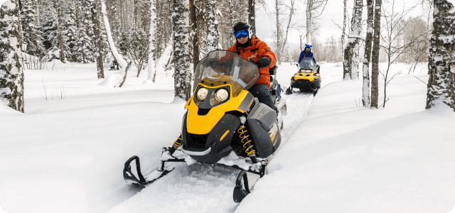 Two people riding snowmobiles separately