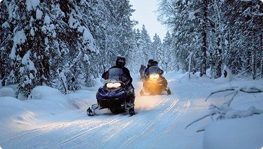 a group of people riding snowmobiles on a snowy road