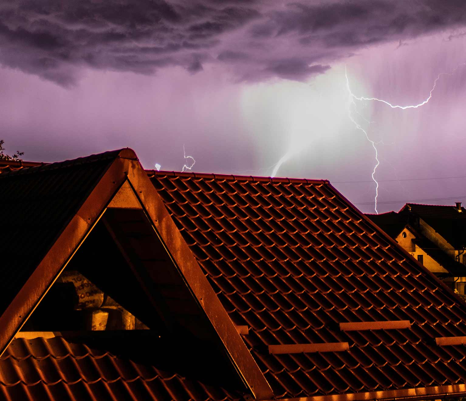Silhouette of roofs with lightning in purple sky.