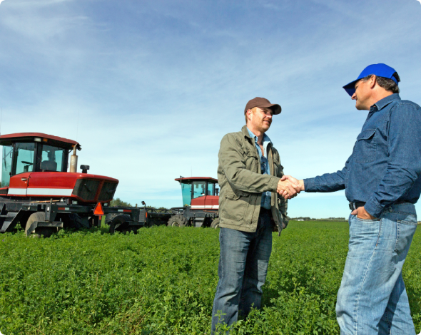 Two men shaking hands on a farm with tractors in the backgroud