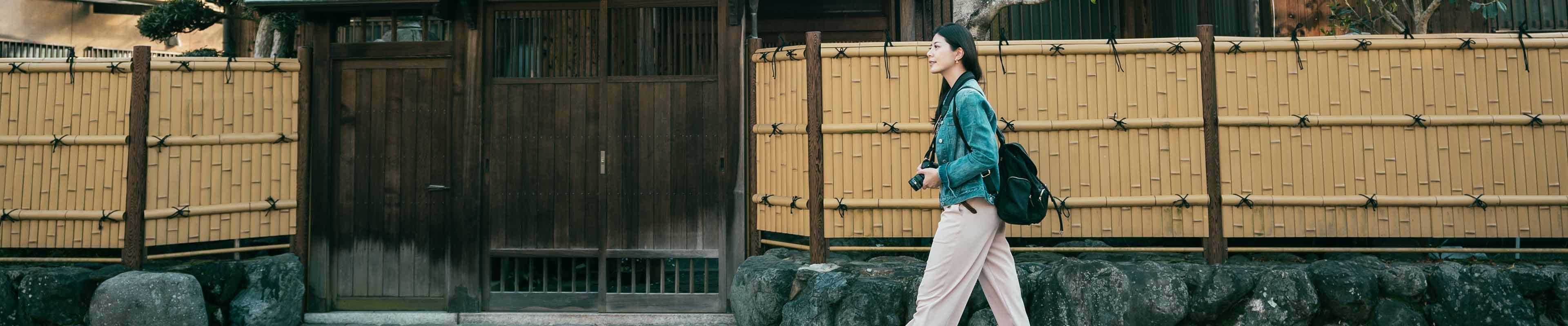 Young Asian woman traveling past a traditional Japanese home while carrying her DLSR camera.